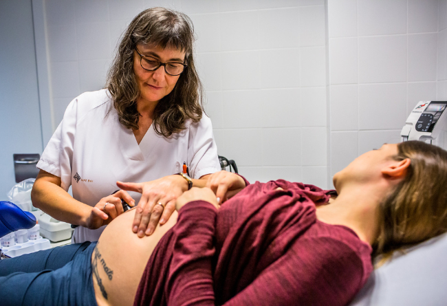 Matrona realiza la auscultación del latido fetal a una mujer embarazada en la consulta (fotografía de Ariadna Creus i Àngel García. Banc d’Imatges Infermeres)